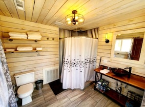 Un baño de cabaña de madera con inodoro, cortina de ducha, lavamanos y espejo.
