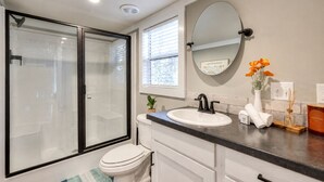 Une salle de bain moderne avec une douche à parois de verre, des toilettes blanches, un lavabo avec un robinet noir et un miroir au-dessus du lavabo.