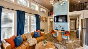 A spacious living area with a leather sofa, a round wooden table, and a dining area with chairs. There is a kitchen with a refrigerator and a TV mounted on the wall. - Cozy Wooden Cabin Surrounded by Trees in Monteagle, Tennessee (Monteagle)