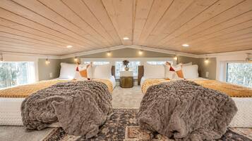 A bedroom with two beds, a wooden ceiling, and a view of trees outside.