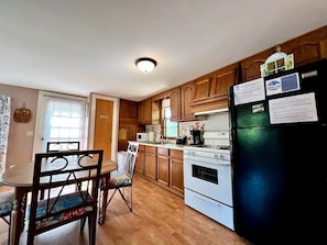 Une cuisine avec des meubles de rangement en bois, un réfrigérateur, une cuisinière et une table à manger avec des chaises.