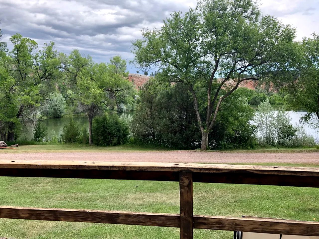 A park with a wooden deck, trees, and a lake.
