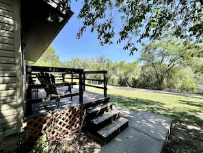 A wooden deck with steps leading to a seating area, surrounded by trees and a clear sky. - Cozy Relaxing Cabin with Lake Views in South Dakota (Hot Springs)