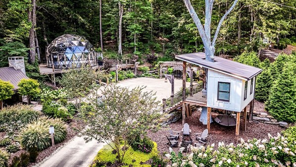 A treehouse with a deck, surrounded by a garden and a dome structure.