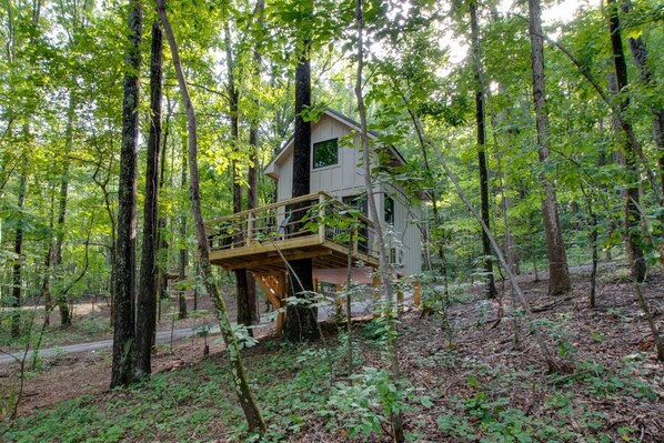 A treehouse with a wooden deck and a single-story structure surrounded by a forest.
