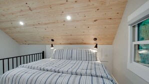 Une chambre avec un plafond en pente, un lit avec une literie à rayures, deux lampes fixées au mur et une fenêtre donnant sur un beau paysage.