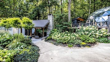 A modern house with a stone chimney, a covered patio, and a garden with various plants.