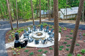 A circular outdoor seating area with chairs and a fire pit, surrounded by trees and a building with a metal roof.