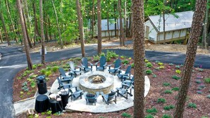 Un espace extérieur circulaire aménagé avec des chaises et un foyer, entouré d’arbres et d’un bâtiment doté d’un toit en métal.