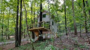 A treehouse with a wooden deck and a single-story structure surrounded by a forest.