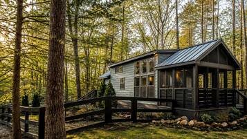 A cabin with a wooden deck, surrounded by trees.