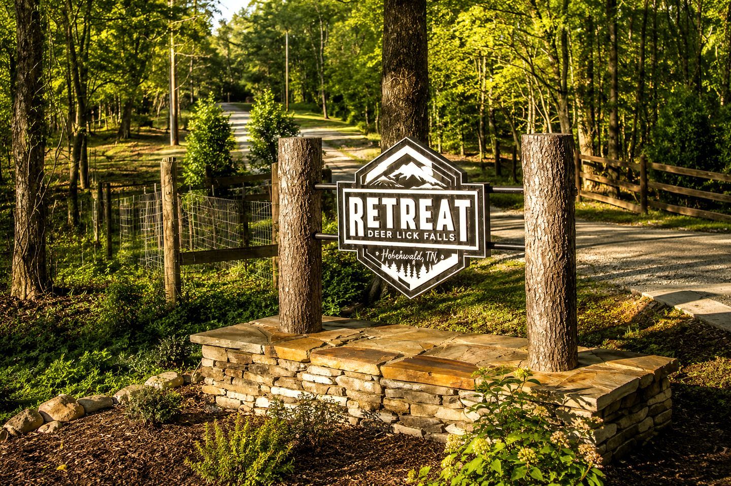 A sign for a retreat named 'Deer Lick Falls' in Hohenwald, TN, surrounded by trees and a stone wall.