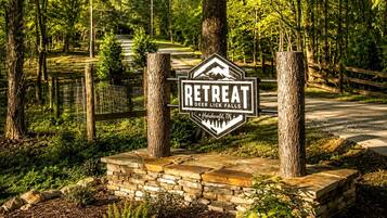 A sign for a retreat named 'Deer Lick Falls' in Hohenwald, TN, surrounded by trees and a stone wall.