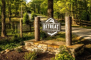 A sign for a retreat named 'Deer Lick Falls' in Hohenwald, TN, surrounded by trees and a stone wall.
