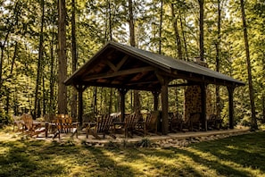 A wooden pavilion with a stone wall, surrounded by chairs and set in a forest.