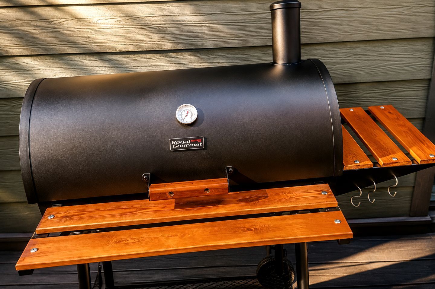 A barbecue grill with a built-in thermometer and a wooden table with metal hooks.