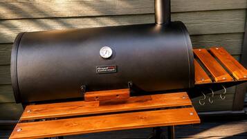 Una parrilla para barbacoa con termómetro incorporado y una mesa de madera con ganchos metálicos.
