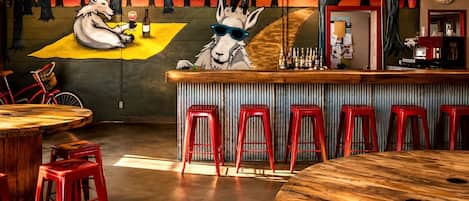 Uma área de bar com um mural de lobos, banquetas vermelhas e um balcão de madeira.
