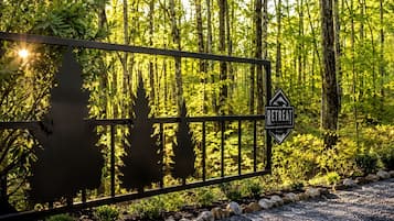 A metal gate with a retreat sign, surrounded by a forested area with trees and a gravel path.