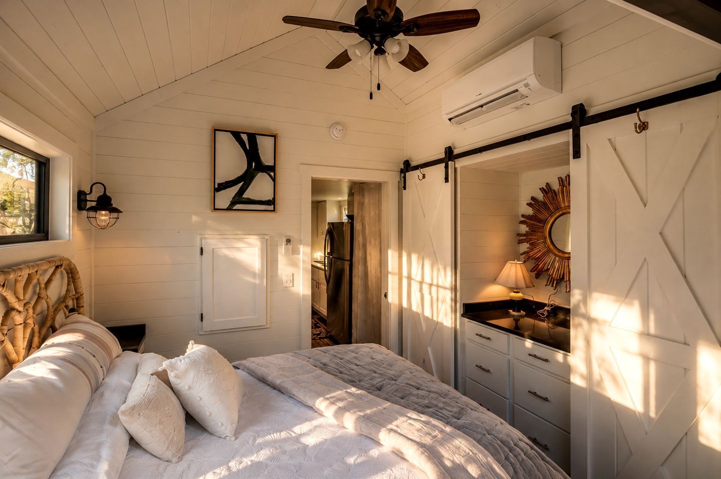 A bedroom with a bed, a ceiling fan, a wall-mounted light, a door, and a mirror.