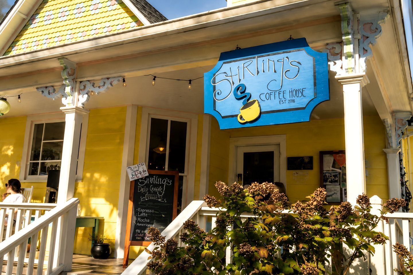 A coffee house with a blue sign, a chalkboard menu, and a porch with a railing.