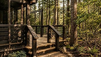 A wooden deck with a staircase leading to a building surrounded by a forest.
