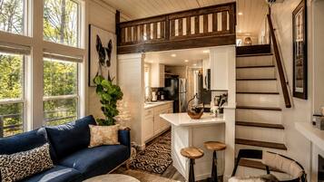 Un intérieur moderne avec un canapé bleu, un coin repas avec des tabourets, une cuisine et un escalier.