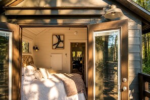 A cozy bedroom with a bed, a door leading to another room, and a window. - Charming Cabin with Stunning Sights in Monteagle, Tennessee (Monteagle)