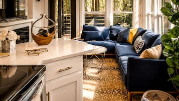 Una sala moderna con sofá modular, espacio de cocina con televisor y un ventanal que ofrece vistas al exterior.