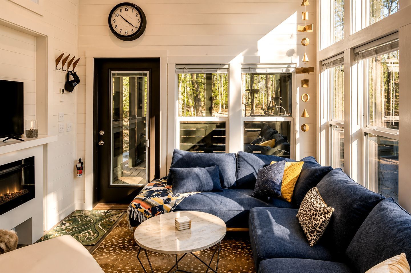 Ein modernes Wohnzimmer mit einem Ecksofa, einem Kamin, einem runden Couchtisch und einem großen Fenster mit Blick ins Freie.