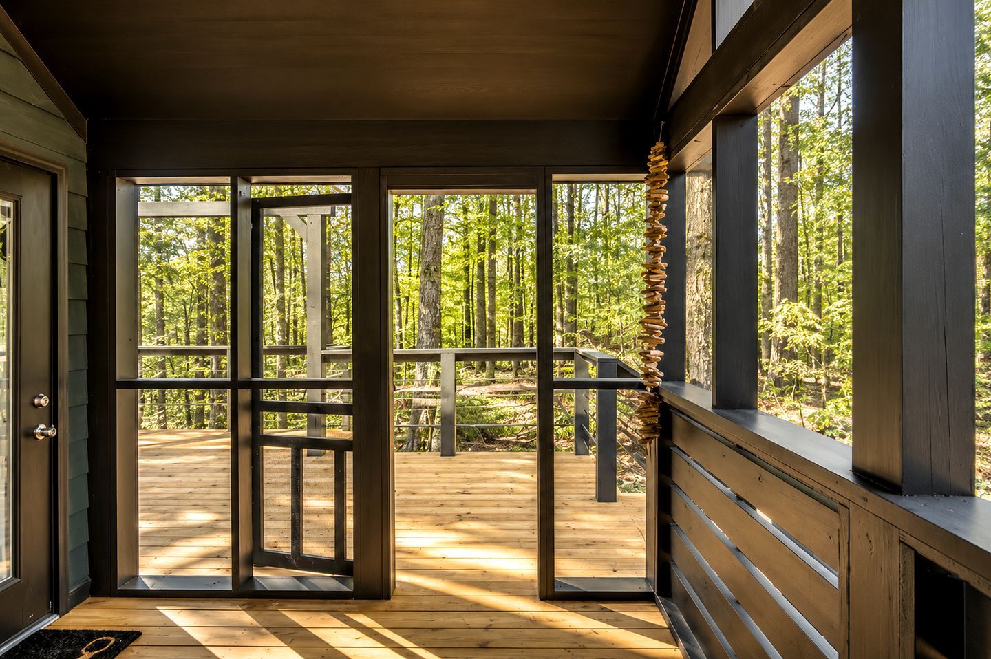 Una terraza de madera con puerta de cristal que da a un área boscosa.