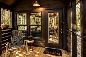 A cozy cabin with a wooden interior, a rocking chair, a small table with a plant, and a 'hello' mat at the entrance.