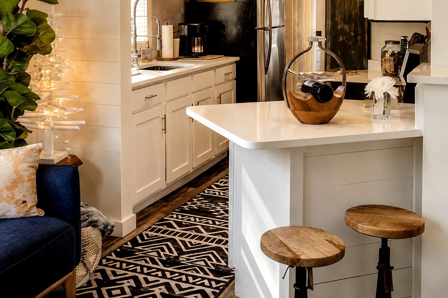 A modern kitchen with white cabinetry, a black refrigerator, and a wooden bar counter with stools.