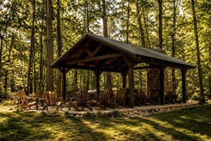 A wooden pavilion with a stone wall, surrounded by chairs and set in a forest. - Charming Cabin with Stunning Sights in Monteagle, Tennessee (Monteagle)
