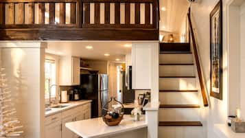 A modern kitchen with white cabinetry, a black refrigerator, and a wooden staircase.