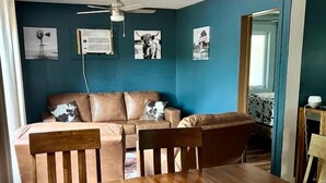 A room with a wooden dining table, a brown leather sofa, and a ceiling fan. - Lakefront Cabin with Deck Great for Families in South Dakota (Hot Springs)