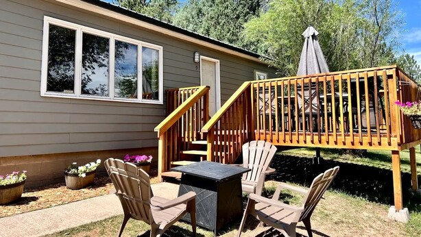 A wooden deck with a table and chairs, a covered area, and a house with large windows.