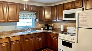 A kitchen with wooden cabinets, a microwave, a refrigerator, a stove, and a window with a view.