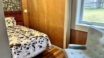 Un dormitorio con una cama, una silla, un ventanal y una puerta de madera.