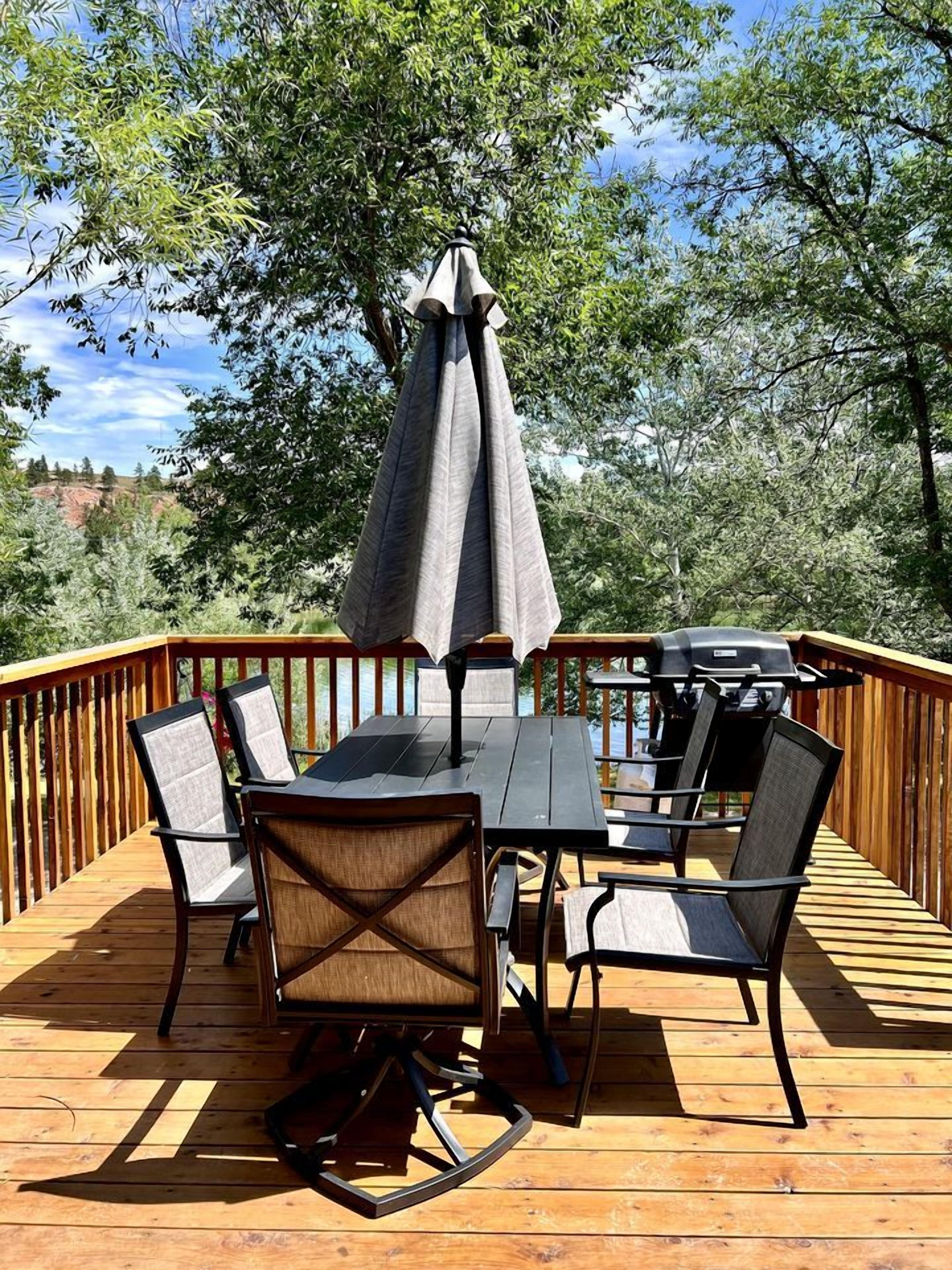A deck with a table and chairs, a grill, and an umbrella.