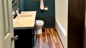 A bathroom with a wooden floor, a white sink, a toilet, and a bathtub.