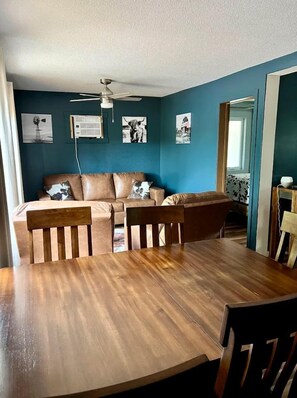 Una habitación con una mesa de comedor de madera, un sofá de cuero marrón y un ventilador de techo.
