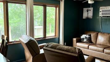 Una habitación con sofá de cuero, sillón reclinable, mesa de comedor y ventilador de techo.