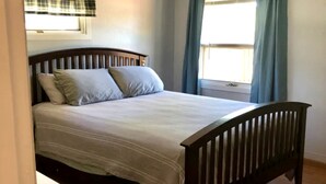A bed with a wooden headboard, two pillows, and a window with curtains. - Lakefront Cabin with Deck Great for Families in South Dakota (Hot Springs)