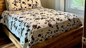 A bed with a cowhide pattern bedspread, a ceiling fan, a wooden headboard, and a cow skull mounted on the wall. - Lakefront Cabin with Deck Great for Families in South Dakota (Hot Springs)