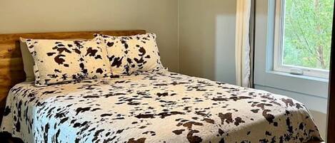 Uma cama com colcha estampada em couro de vaca, um ventilador de teto, uma cabeceira de madeira e um crânio de vaca fixado na parede.