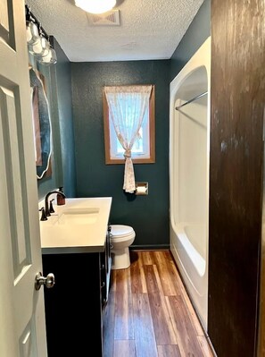 A bathroom with a wooden floor, a white sink, a toilet, and a bathtub. - Lakefront Cabin with Deck Great for Families in South Dakota (Hot Springs)