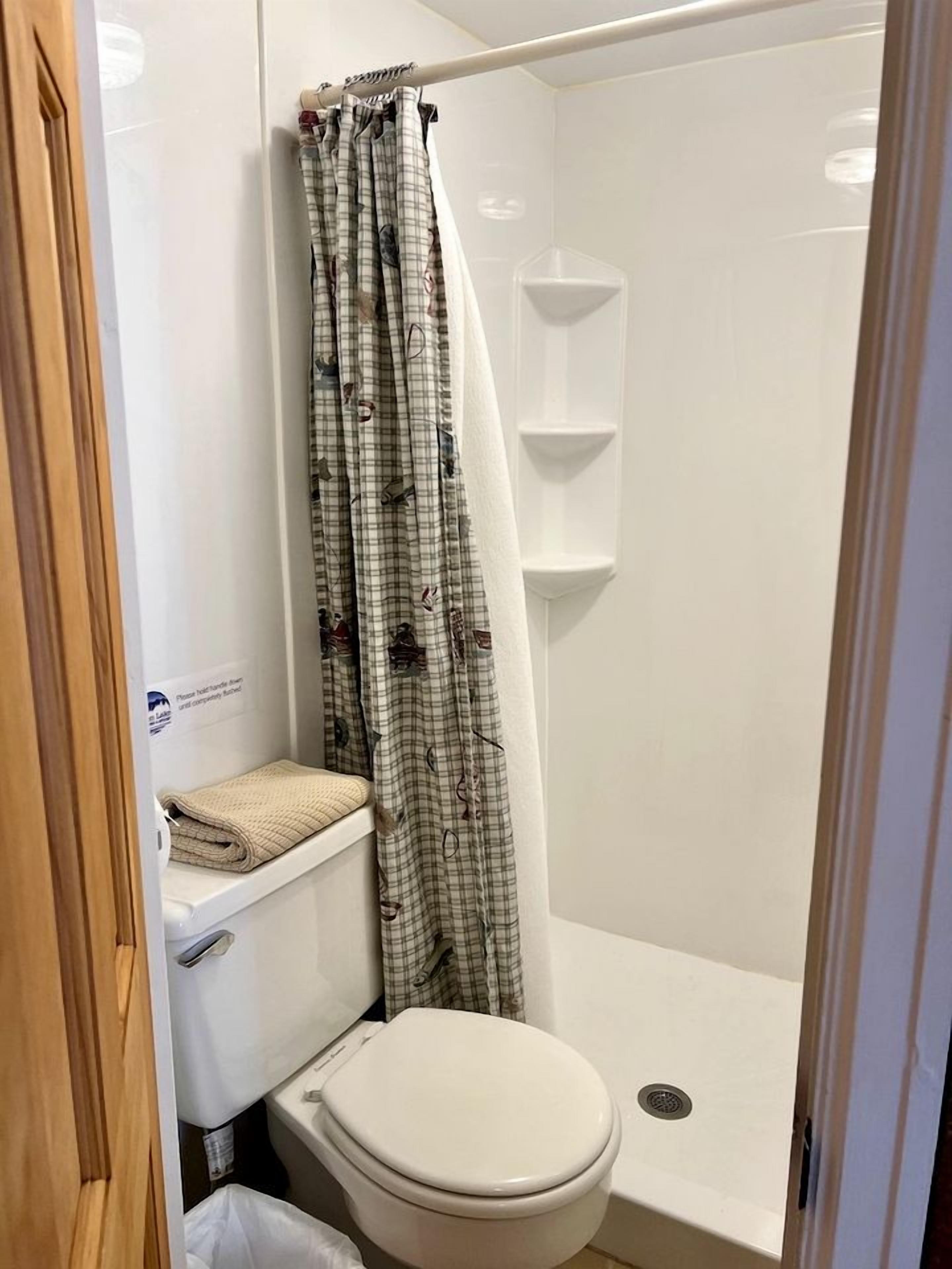 Un baño pequeño con inodoro, zona de ducha y estante.