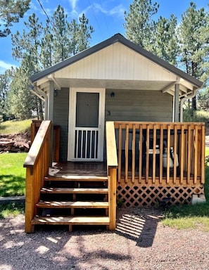 A small cabin with a wooden deck, a front door, and a number '3' on the wall.