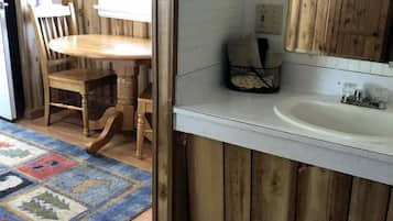 Un interior de madera con una mesa de comedor, sillas, un lavamanos blanco y una alfombra estampada.